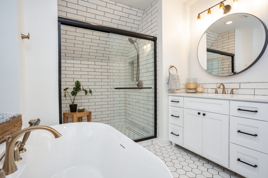 Full bath with white furniture-style vanity, soaker bathtub, tile shower with white subway tile, hexagonal white floor tile.