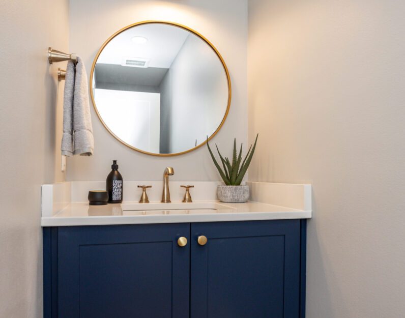 Remodeled powder bathroom with blue vanity and white quartz counters, gold fixtures.