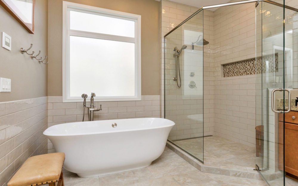A bathtub next to the shower area and beside the window